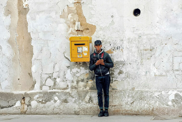 Young man standing beside a yellow mailbox on a weathered wall, capturing the beauty of everyday life in India by street photographer.