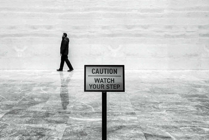 A street photographer captures a man walking past a caution sign in a minimalist urban setting in India.