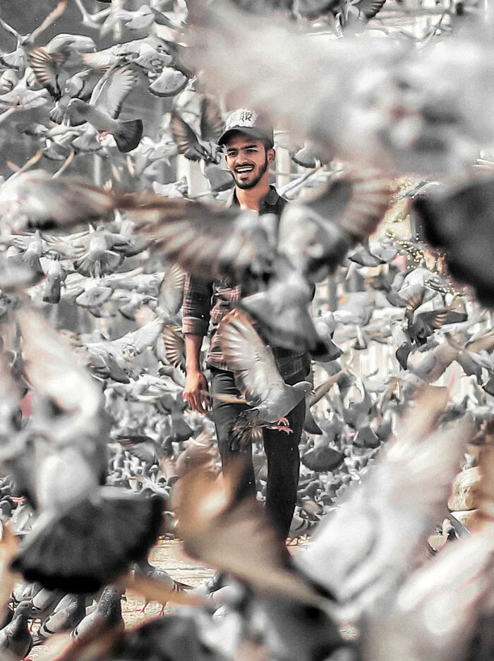 Young man smiling amidst a flock of pigeons, capturing the beauty of everyday life in India by street photography.