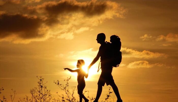 Silhouettes of a man and two children walking at sunset, capturing beautiful photos of childhood around the world.