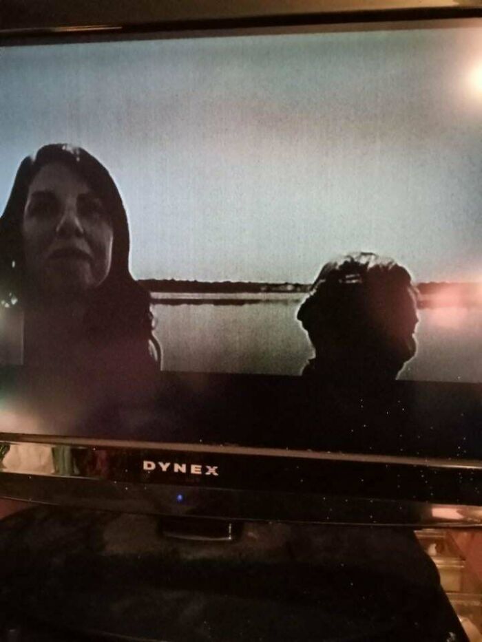 Two dark silhouettes of people on a TV screen creating an unexplained eerie visual effect by the water.