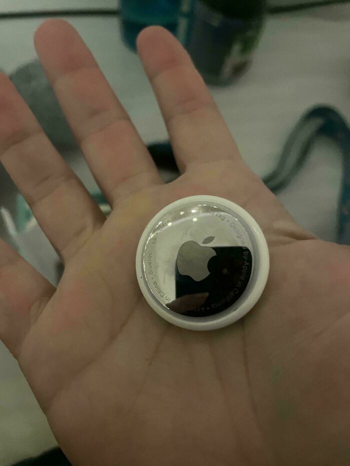 Hand holding an Apple AirTag device, a small circular item that some things just cannot be explained.