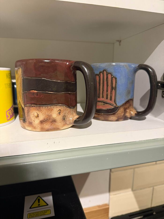 Two unique ceramic mugs with unusual designs sitting on a kitchen shelf, highlighting some things that cannot be explained.