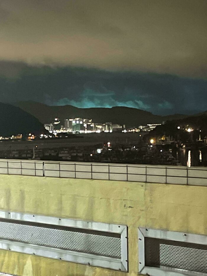 Nighttime cityscape with mysterious glowing blue light over distant hills in an unexplained interesting group photo.