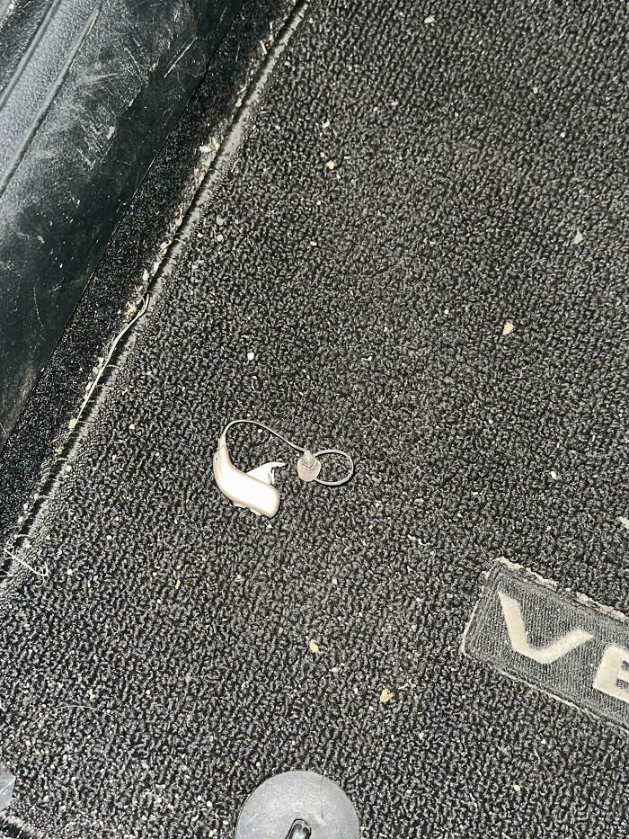 Small silver earpiece lying on a textured black car floor mat, showcasing interesting unexpected find from this group.