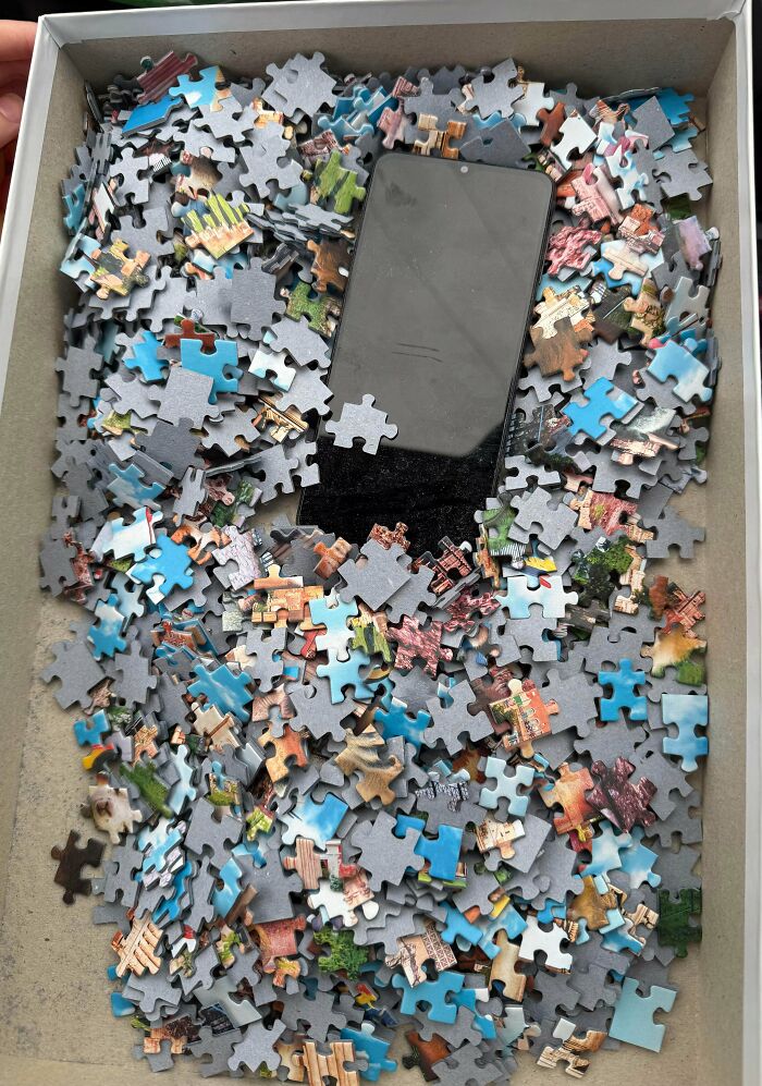Smartphone partially buried in a box filled with colorful jigsaw puzzle pieces, highlighting interesting group moments.