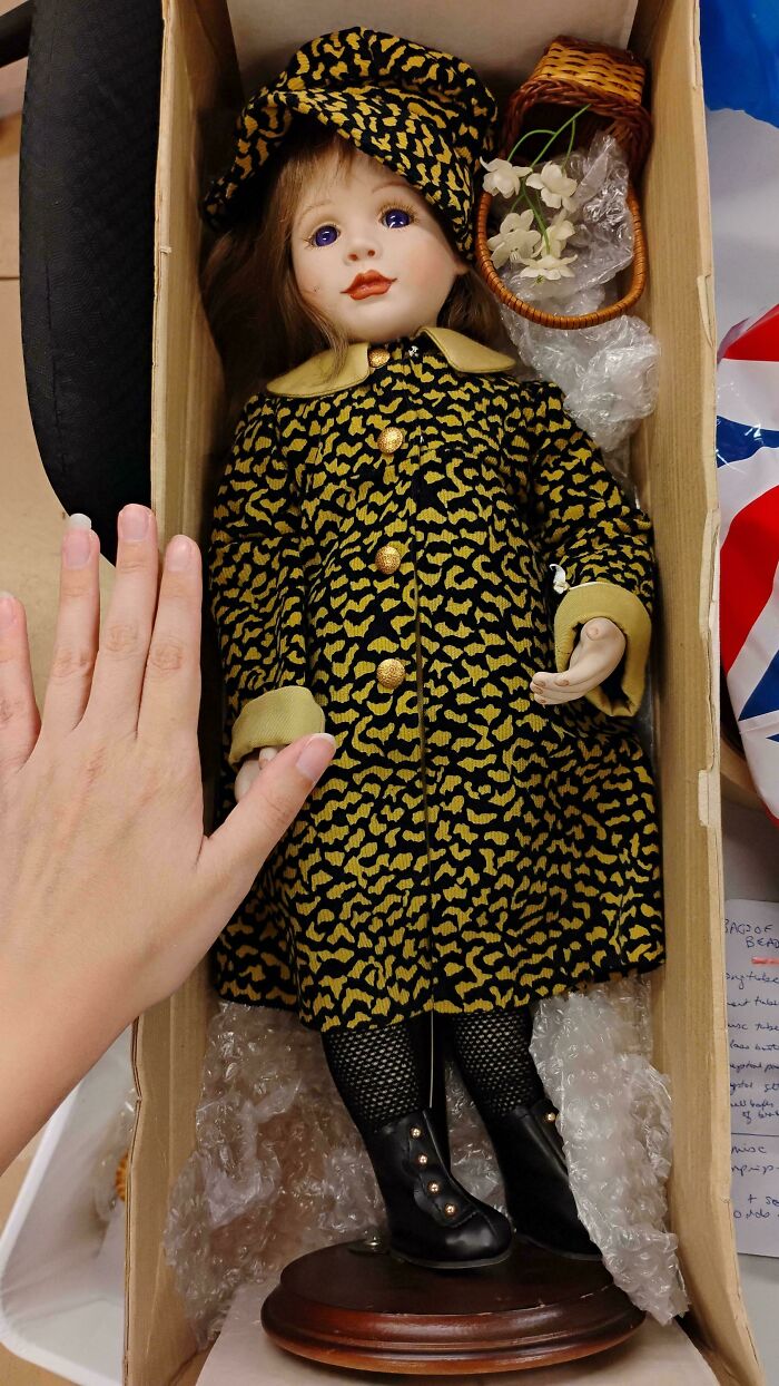 Porcelain doll with purple eyes in a patterned coat and hat lying in a box, part of interesting group collection.