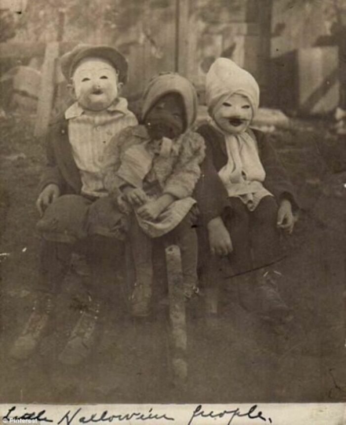 Three children sitting outdoors wearing vintage Halloween costumes and creepy masks from the past Halloween costumes.