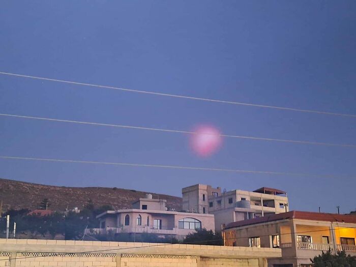 Pink glowing orb floating above buildings at dusk, an unexplained phenomenon captured in this interesting group photo.