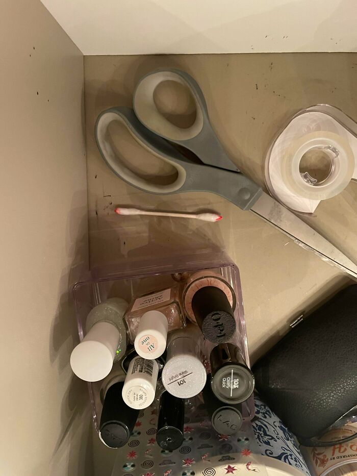Nail polish collection with scissors, tape, and a cotton swab on a beige vanity surface, showing unexplained arrangement.