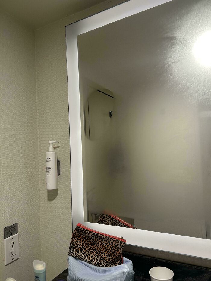 Fogged bathroom mirror reflecting a faint figure, with toiletries and a leopard print bag on the counter in an unexplained scene.