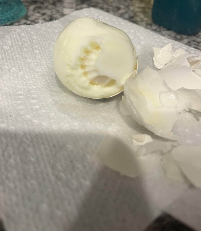 Partially peeled hard-boiled egg showing an unusual indentation on a white paper towel, highlighting unexplained oddities.