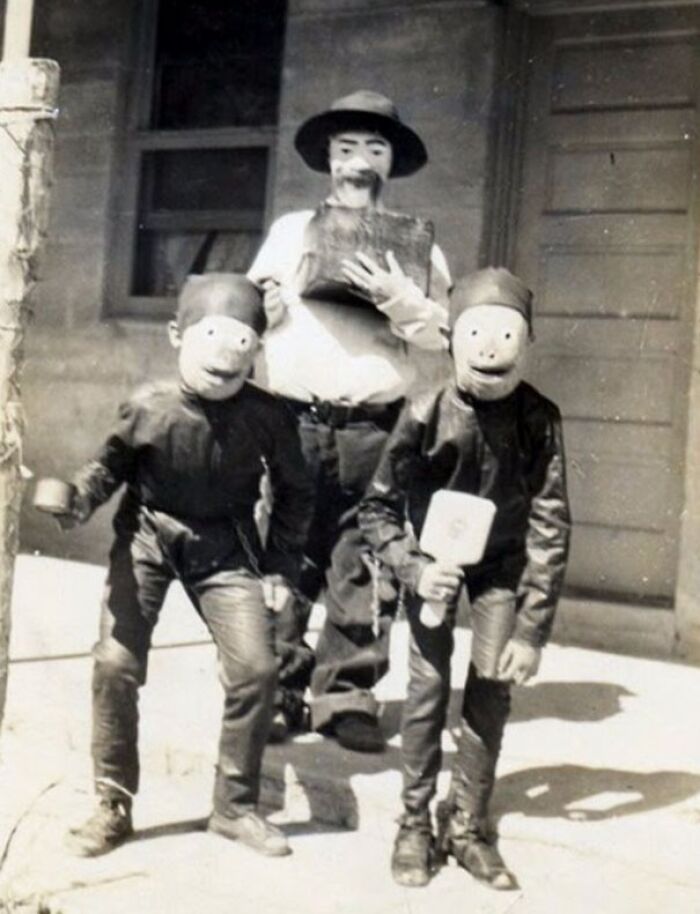 Three people wearing vintage Halloween costumes with large masks and dark outfits, showcasing old Halloween costumes.