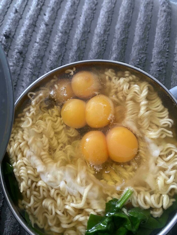 Close-up of ramen noodles with multiple egg yolks and greens in a bowl, showing a unique food moment that cannot be explained.