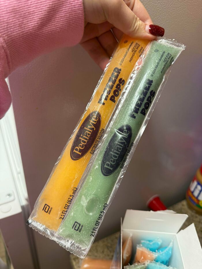 Hand holding two Pedialyte freezer pops in orange and green colors, illustrating interesting group products.