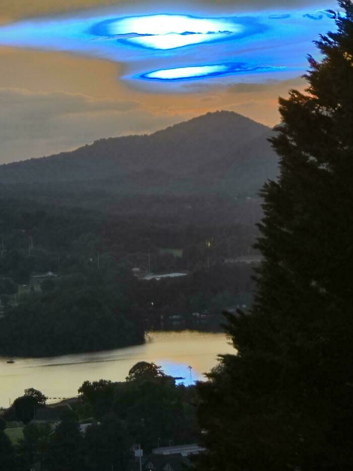 Unexplained glowing blue rings in the sky above a mountain landscape during sunset, reflecting on a river below.
