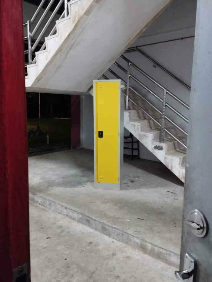 Yellow locker placed oddly under concrete stairs in a dimly lit area, illustrating unexplained interesting group moments.