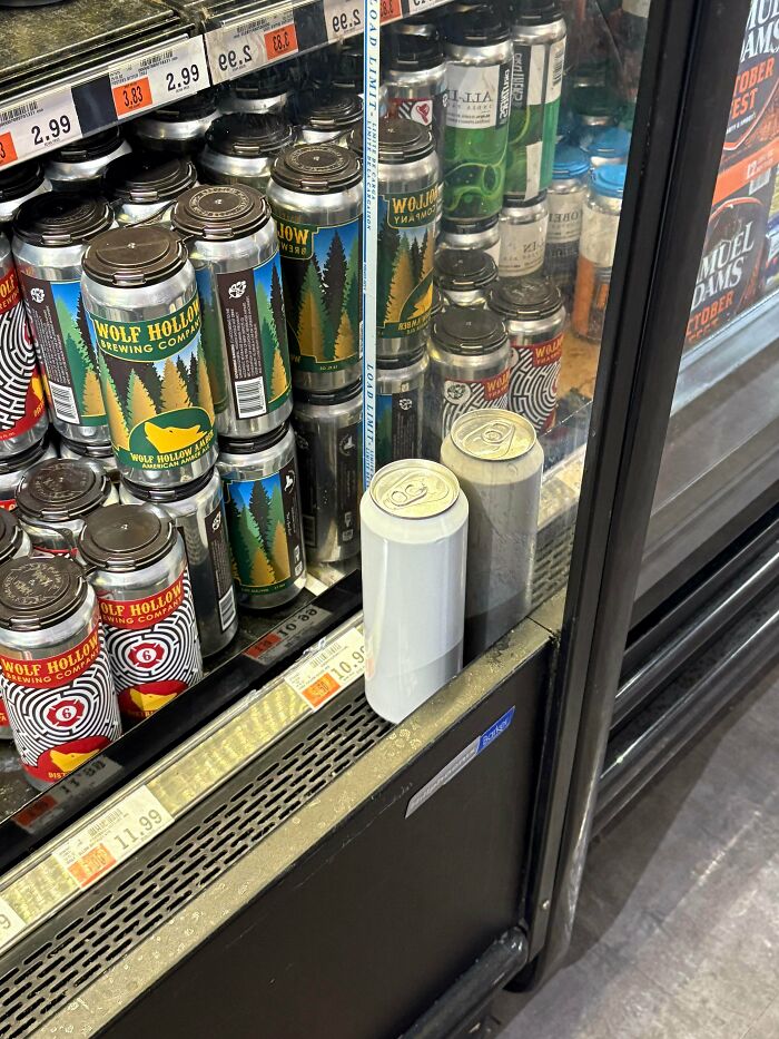 Two silver cans placed outside a refrigerated section with Wolf Hollow Brewing Company beers inside, an unusual sight.