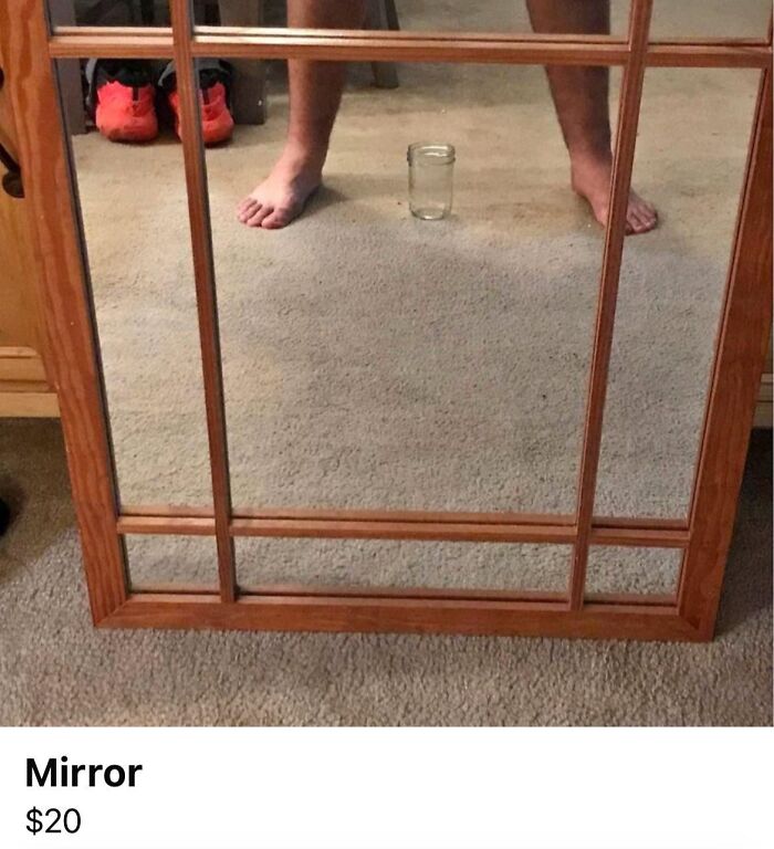 Wood framed mirror reflecting bare feet and a glass jar on carpet, showcasing a humorous angle for mirror sale.
