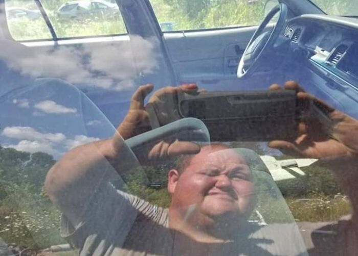 Reflection of a man taking a photo through a car window, demonstrating a humorous mirror selling fail with reflection selling it.