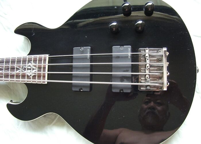 Black electric guitar with glossy finish showing reflection of a shirtless man, illustrating mirror reflection selling humor.