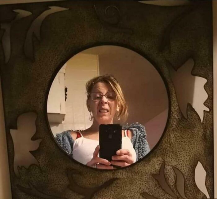 Woman taking a selfie in a decorative mirror for sale with emphasis on the reflection selling the mirror online.
