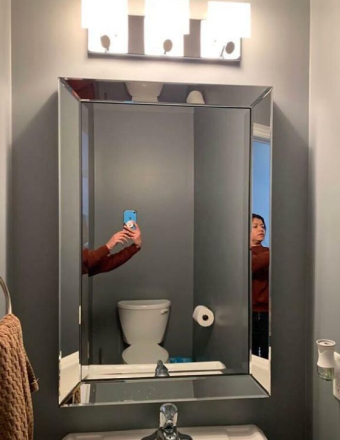 Bathroom mirror reflecting a person taking a photo with a toilet and towel visible, highlighting funny mirror reflection selling moments.