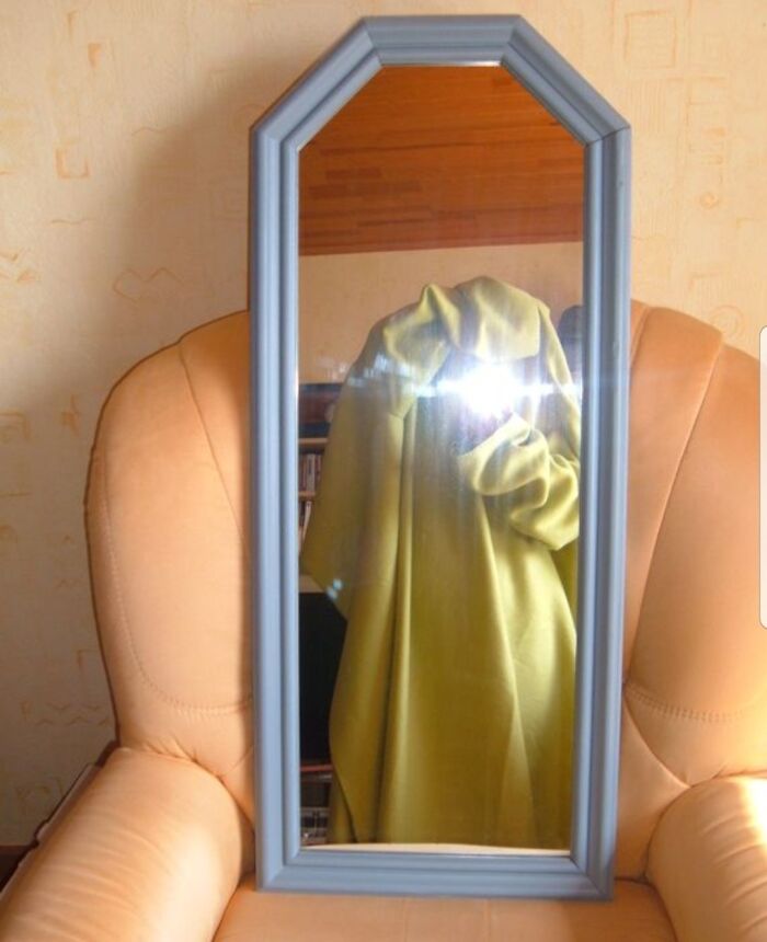 Mirror photo shows reflection of person in green cloak with flash light obscuring face, highlighting hilarious mirror sale moments.