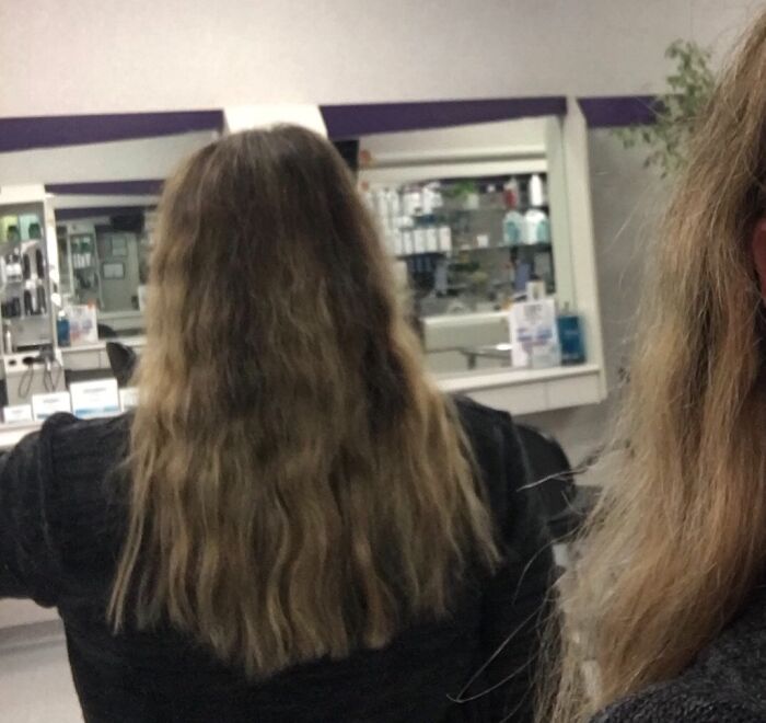 Woman in a salon with long wavy hair showing a humorous hair accident in the mirror reflection.