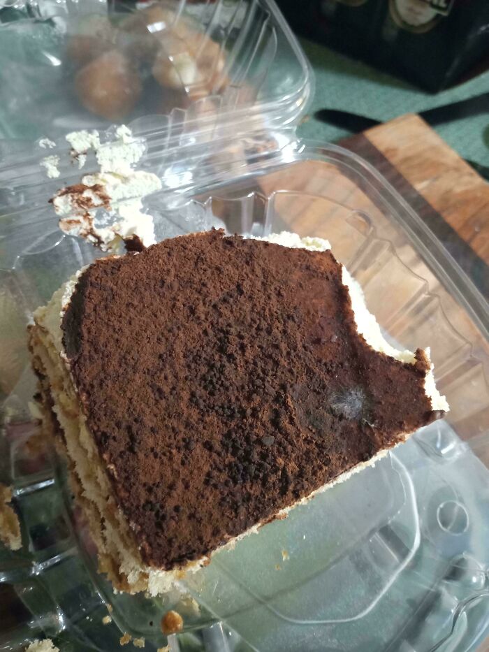 Partially eaten dessert with mold growing on the chocolate topping in a clear plastic container illustrating mess and neglect.