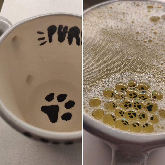 Close-up view of a cup with a painted paw print inside, revealed by bubbles floating on a drink surface.