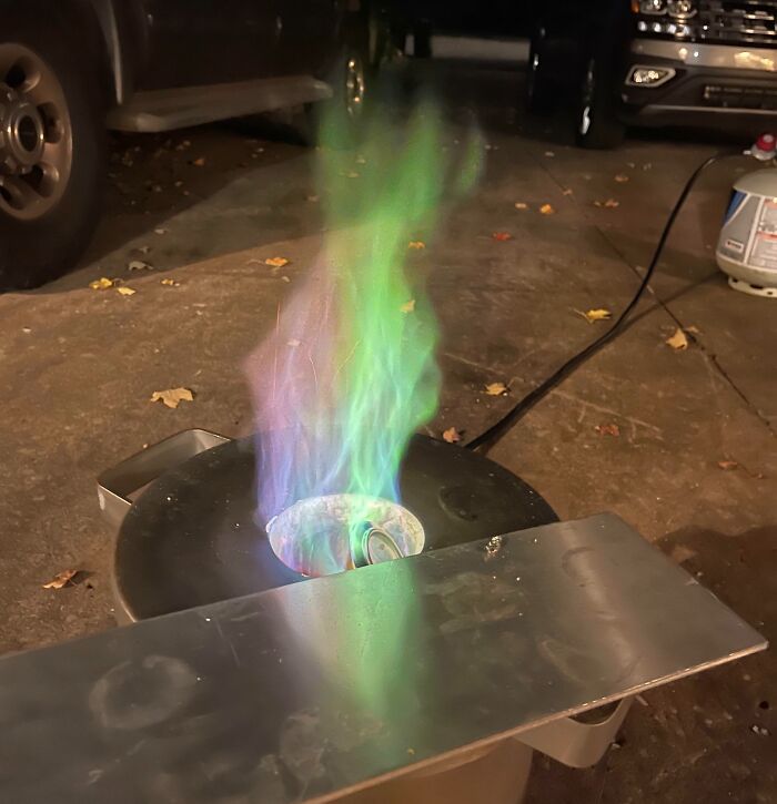 Multicolored flame rising from a metal container in a garage setting showcasing interesting pics with unique visual questions.