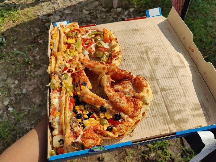 Partially eaten messy pizza with various toppings in a stained box, illustrating a total mess scene outdoors.