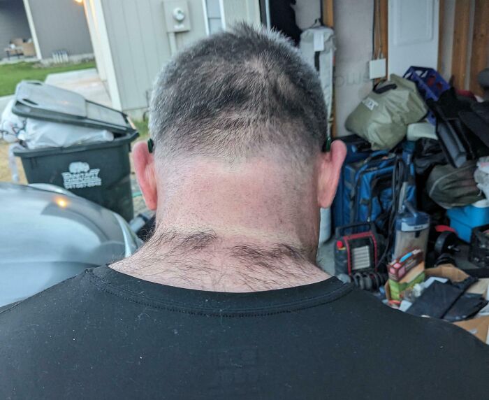 Man with uneven, patchy hair and tragic hair accidents visible on the back of his head in a cluttered garage setting