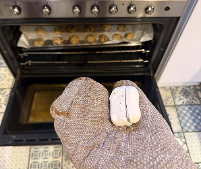 Oven mitt holding burnt AirPods case with cookies baking inside oven, illustrating a total mess day concept.