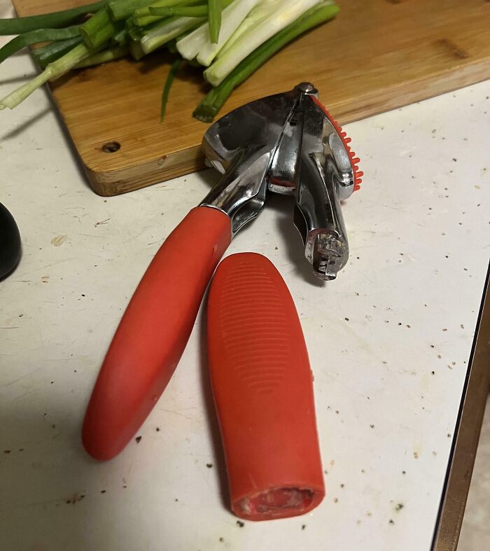 Red-handled kitchen tool with broken metal garlic press part on a messy countertop showing total mess scene.