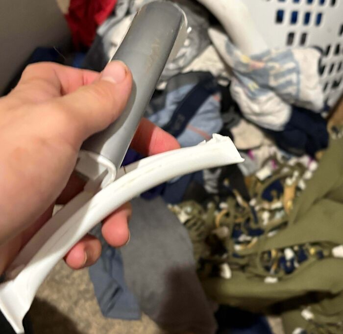 Hand holding a broken plastic item with a messy pile of clothes in the background, showing a total mess moment.