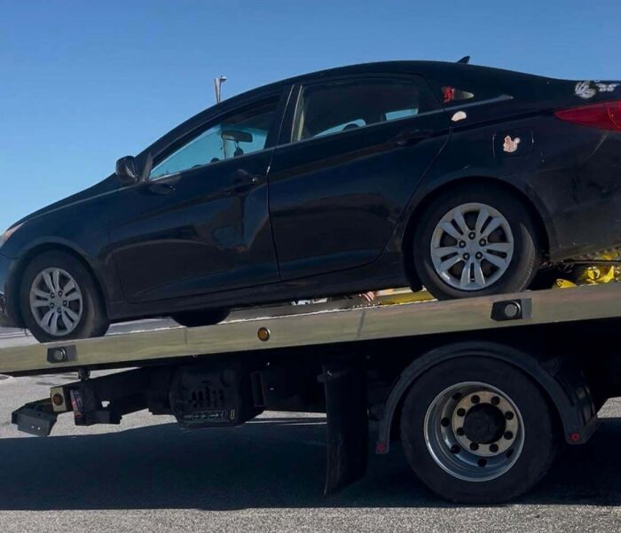 Black car with visible body damage being towed on a flatbed truck, illustrating a total mess and worse situations.