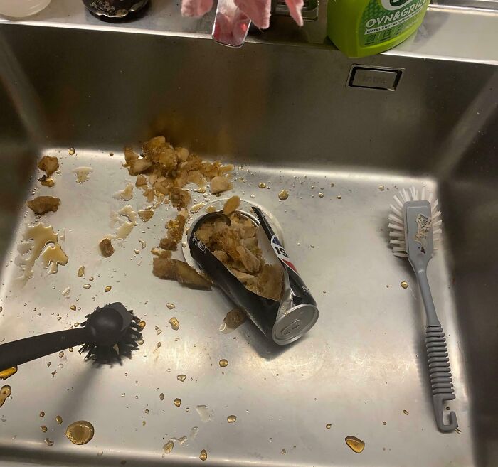 Crushed can with spilled liquid and food debris in a kitchen sink, illustrating a messy and chaotic moment.