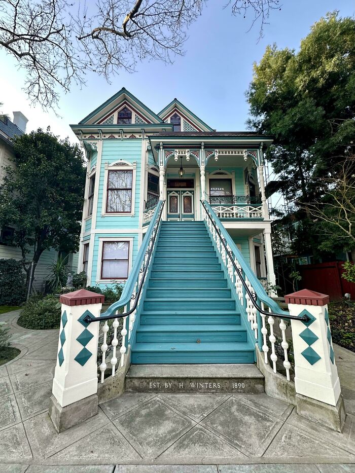 Victorian charming old home with teal exterior, intricate woodwork, and a grand staircase leading to the porch entrance.