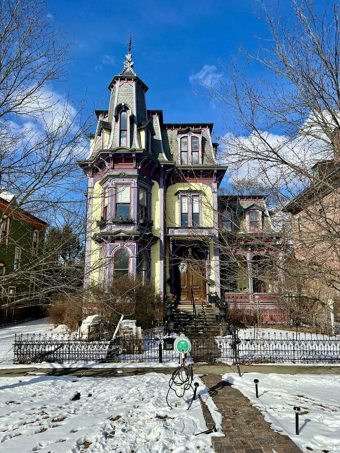 Victorian charming old home with intricate details and a fenced yard surrounded by winter trees under a blue sky.