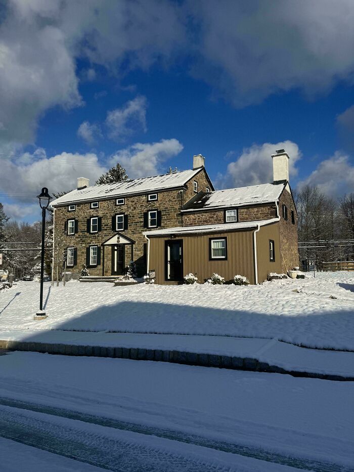 Charming old stone house covered in snow under a blue sky, showcasing historic architecture and winter scenery.