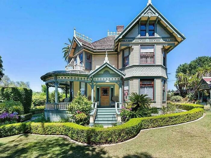 Victorian charming old home with detailed woodwork, wraparound porch, and well-maintained garden under a clear blue sky.