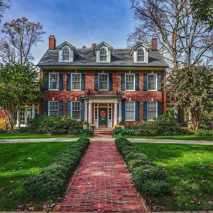 Charming old home with brick exterior and classic windows surrounded by green lawn and trees under blue sky.