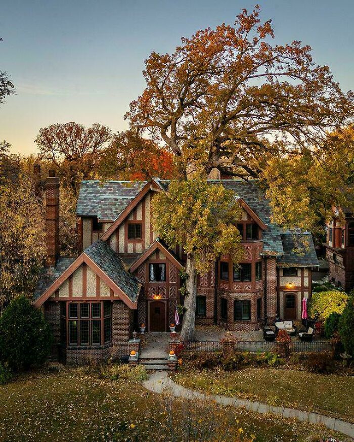 Charming old home with brick exterior and steep roof surrounded by autumn trees in a peaceful residential setting