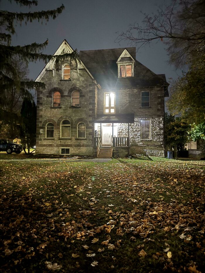 Charming old home at night with lit windows and fallen autumn leaves on the lawn, showcasing historic architecture details.