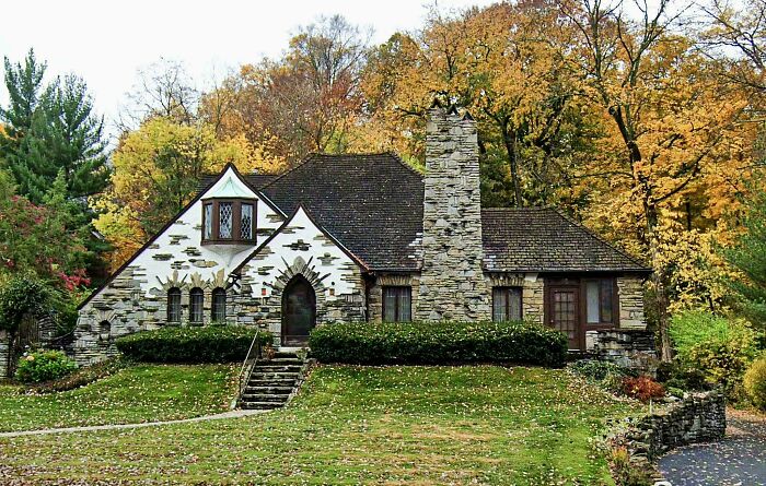 Charming old home with stone chimney and detailed windows surrounded by autumn trees in a picturesque setting.