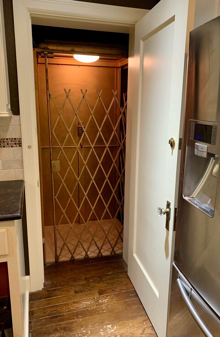 Old home interior showing vintage elevator with metal gate, wooden floor, and modern kitchen appliances nearby.