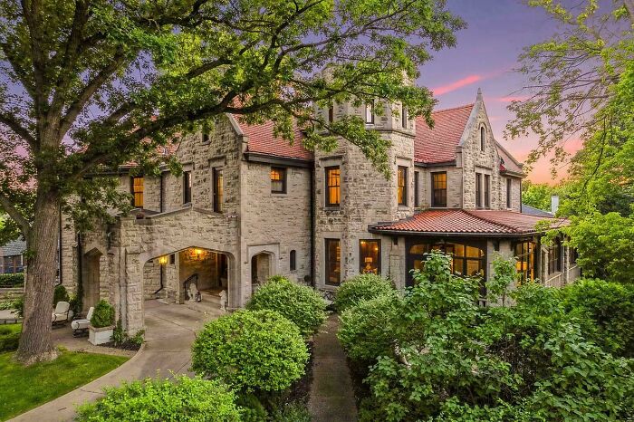 Charming old stone home surrounded by lush greenery and trees at sunset, showcasing timeless architectural details.