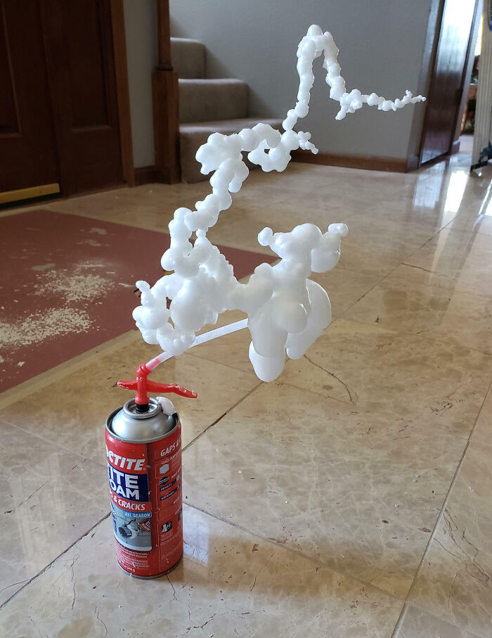 Expanding foam leaking from aerosol can, forming unusual shapes on a tiled floor in a home setting.